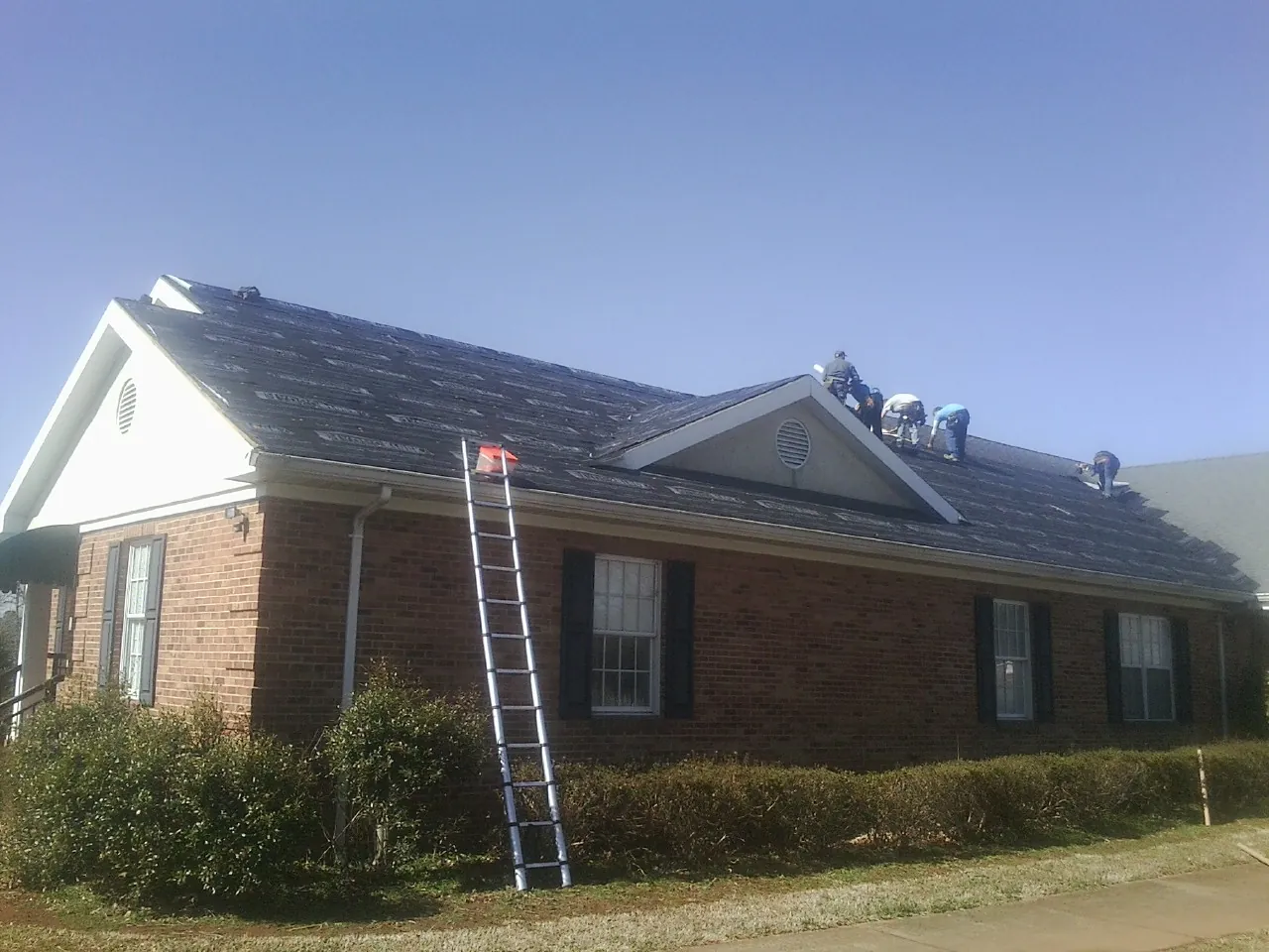 Crew tearing shingles off a brick ranch roof with a ladder set — Emergency Roof Repair work by our crew in Reading
