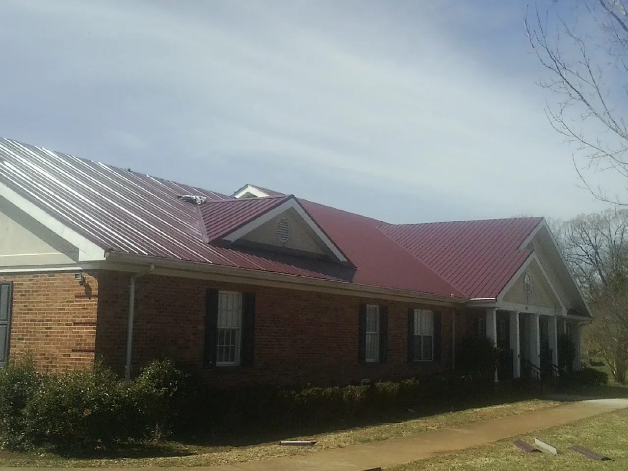Red metal roof with gabled entries on a long brick building, from a Hail Damage Roof Repair job in Reading